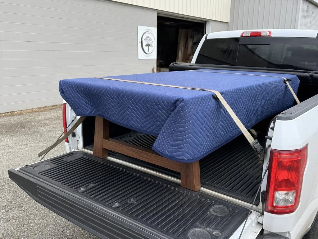 Finished table wrapped in moving blankets strapped into a pickup truck